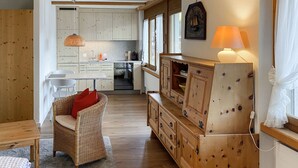 Una cocina acogedora con armarios de madera, un comedor con una silla de mimbre y una lámpara sobre un mueble de madera.