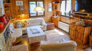 Een gezellig chaletinterieur met houten wanden, een bank, een eettafel, een televisie en een open haard.
