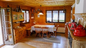 Een houten hutinterieur met een eettafel, stoelen, een keuken en een groot raam.