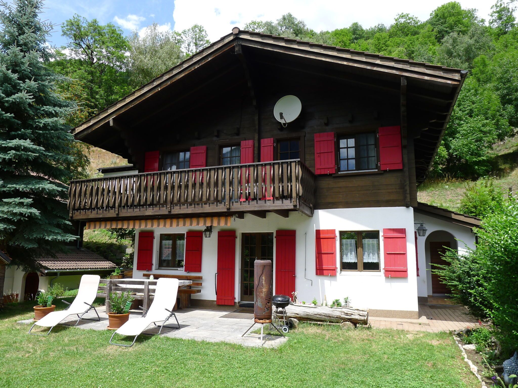 Eine zweistöckige Chalet mit Balkon, roten Fensterläden und einer Satellitenschüssel.