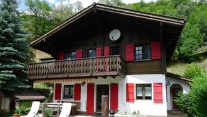 Een chalet met twee verdiepingen, een balkon, rode luiken en een schotelantenne.