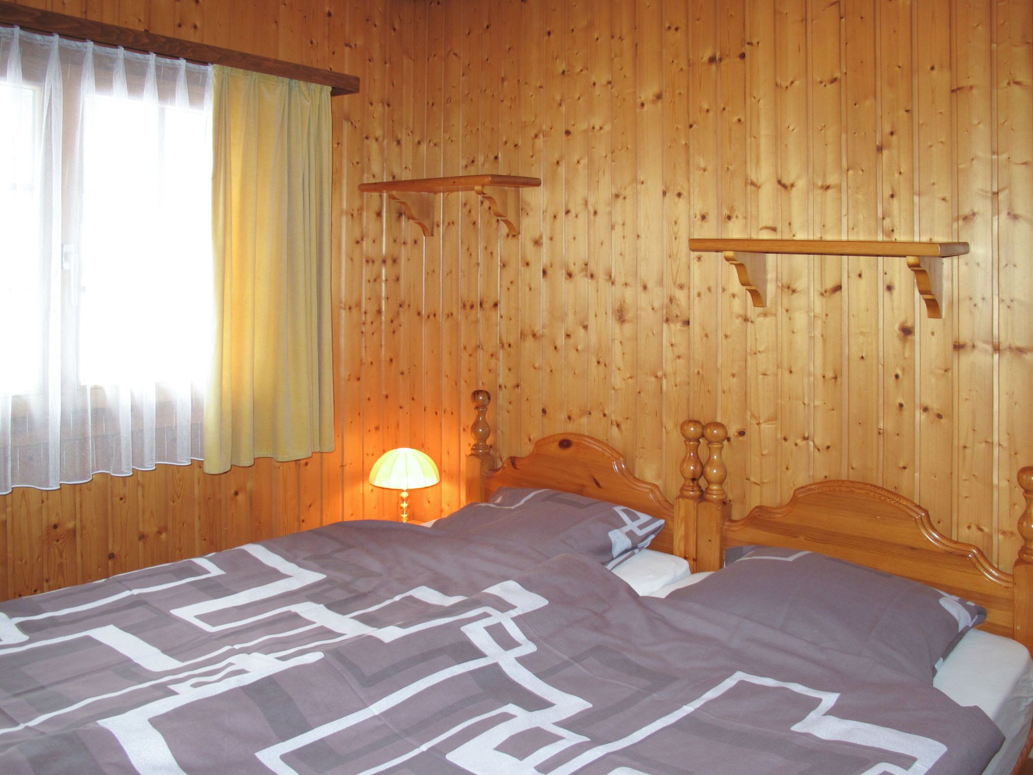 Una habitación con paneles de madera, una cama, una mesita de noche y una lámpara.