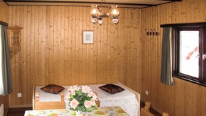 Ein Zimmer mit Holzwänden, zwei Einzelbetten mit Kissen, einem Tisch mit Blumenmuster-Tischdecke, einer Blumenvase und einer Hängelampe.