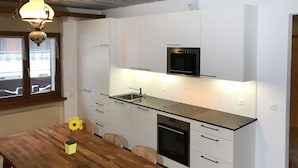 Una cocina moderna con armarios blancos, horno empotrado y microondas negro. Hay una mesa de madera con un florero de flores amarillas.