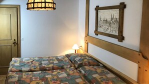 Un dormitorio con cabecera de madera, colcha acolchada, cuadro enmarcado de un paisaje urbano, lámpara colgante y mesita de noche con lámpara.