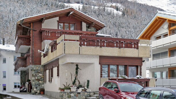 A two-story building with a stone facade, wooden balconies, and a red car parked in front. - Haus Quelle by Interhome (Saas-Grund)