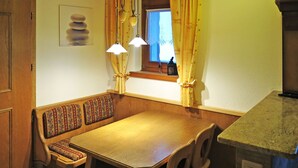 Ein gemütlicher Essbereich mit Holztisch und Bank, einem Fenster mit Vorhängen und Pendelleuchten.