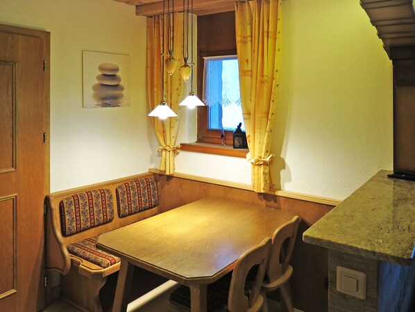 A cozy dining area with a wooden table and bench, a window with curtains, and pendant lights.