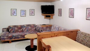 Ein Wohnzimmer mit einer Couch, einem kleinen Tisch und einem an der Wand befestigten Fernseher.