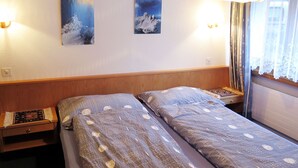 Ein Hotelzimmer mit zwei Betten, einem Holzkopfteil, einem Nachttisch, einer Lampe und zwei Wandgemälden.