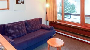A room with a sofa, a small wooden stool, a window with curtains, and a framed picture on the wall.