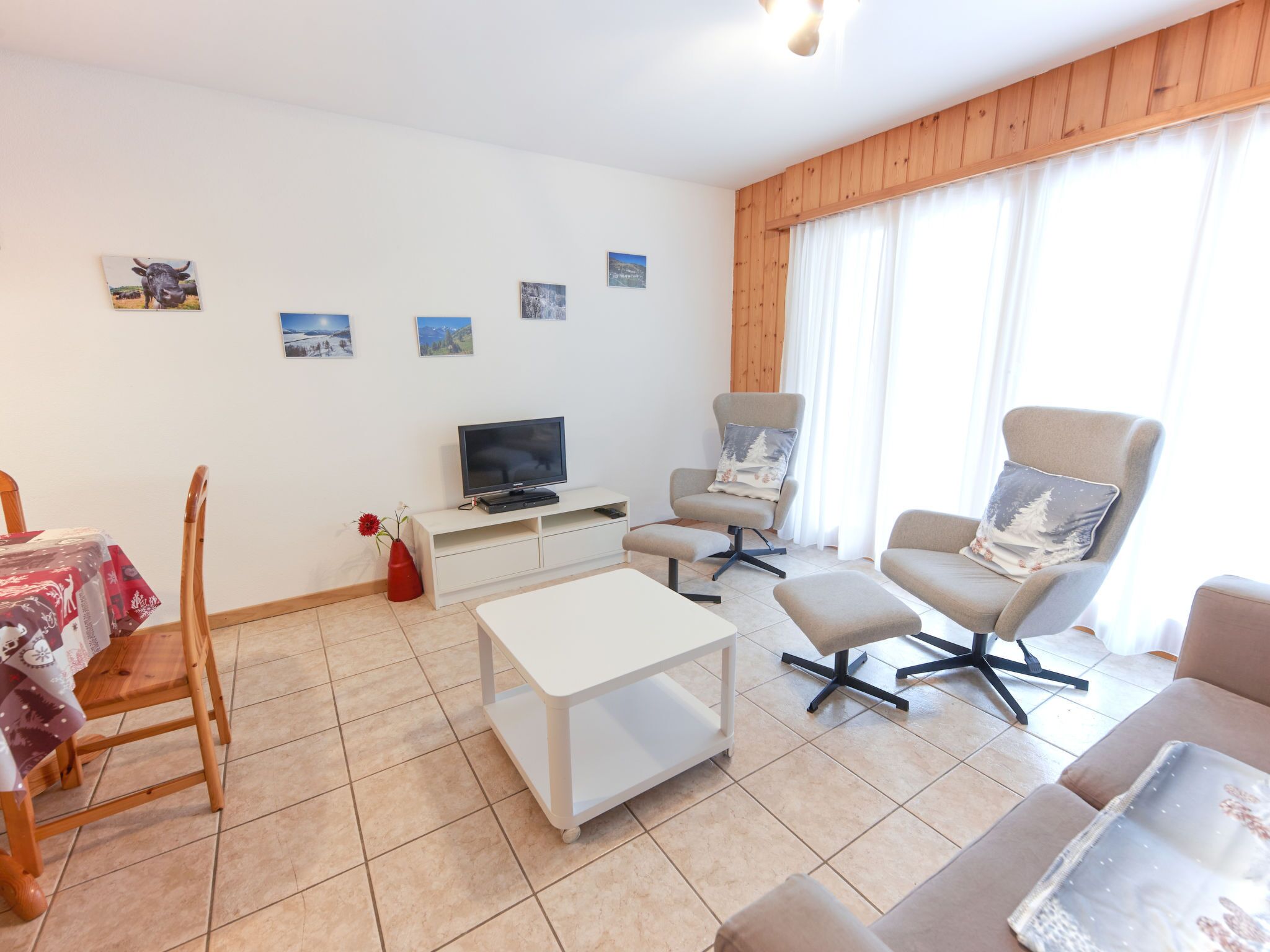 A modern living room with a flat-screen TV, two armchairs, a sofa, a coffee table, and a dining table with chairs.