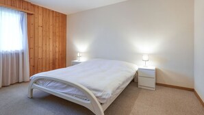 A bedroom with a bed, two bedside tables, a wooden wall panel, and a window with curtains.