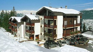En fleretages hytte med altaner og en skibakke i baggrunden.