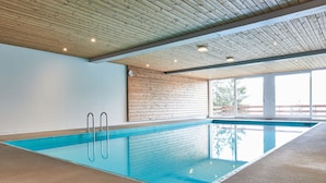 An indoor swimming pool with wooden ceiling beams, a brick wall, and a large window. - Hameau D01 by Interhome (Thyon-Les Collons)