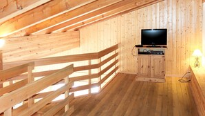 En stuga med träpanel på insidan, utrustad med en tv, en träbänk och en lampa.