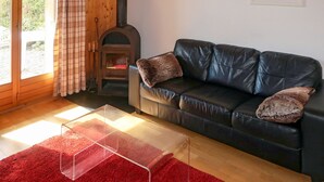A cozy living room with a black leather sofa, a red rug, and a wood-burning stove.