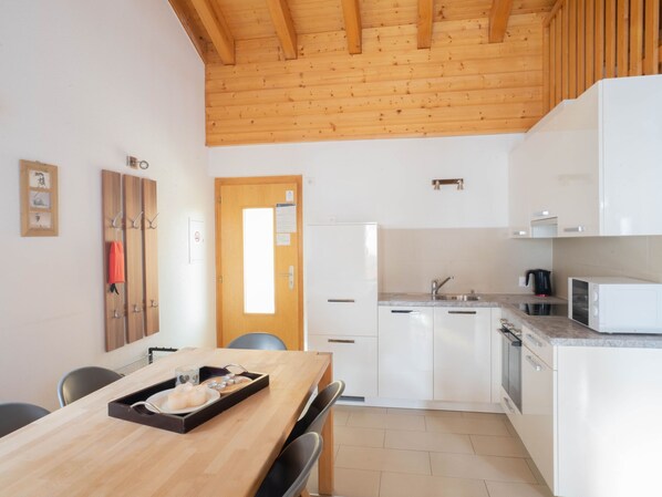 A modern kitchen with white cabinets, a wooden ceiling, and a dining area with a wooden table and chairs. - Apartment Grives by Interhome (Thyon-Les Collons)