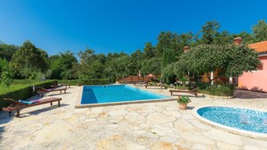 A rectangular swimming pool with a stone deck, surrounded by lounge chairs and a small circular pool.