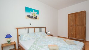 A bedroom with a wooden bed, a nightstand with a lamp, a wardrobe, and a painting on the wall.