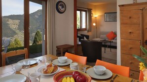 A dining area with a table set for breakfast, a view of the outdoors, and a cozy living room in the background. - Edelweiss by Interhome (La Tzoumaz)