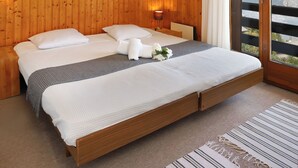 A wooden-paneled bedroom with a large bed, white bedding, a bedside lamp, and a view of mountains through a sliding door. - Edelweiss by Interhome (La Tzoumaz)