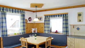 A cozy dining area with a wooden table and bench seating, a ceiling fan, and a kitchen area with cabinets and a window. - Apartment Margit by Interhome (Haus)