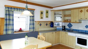 A kitchen with wooden cabinets, a microwave, a sink, and a dining area with a table and chairs. - Apartment Margit by Interhome (Haus)
