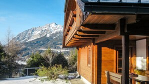A wooden cabin with a wooden deck and a bench, surrounded by snow and mountains in the background. - Simons Blockhütte by Interhome (Gröbming)