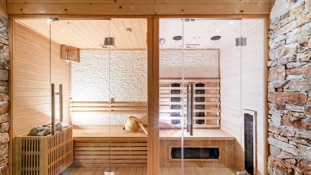 A sauna room with wooden benches, a stone wall, and a glass door. - Simons Blockhütte by Interhome (Gröbming)