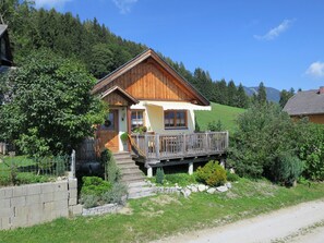 Eine Holzhütte mit Balkon, umgeben von viel Grün und Bergen.