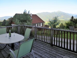 Eine Holzterrasse mit Tisch und Stühlen, mit Blick auf eine gebirgige Landschaft.