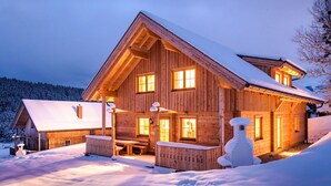 Una cabaña de madera con techo inclinado, ventanas amplias y exterior cubierto de nieve.