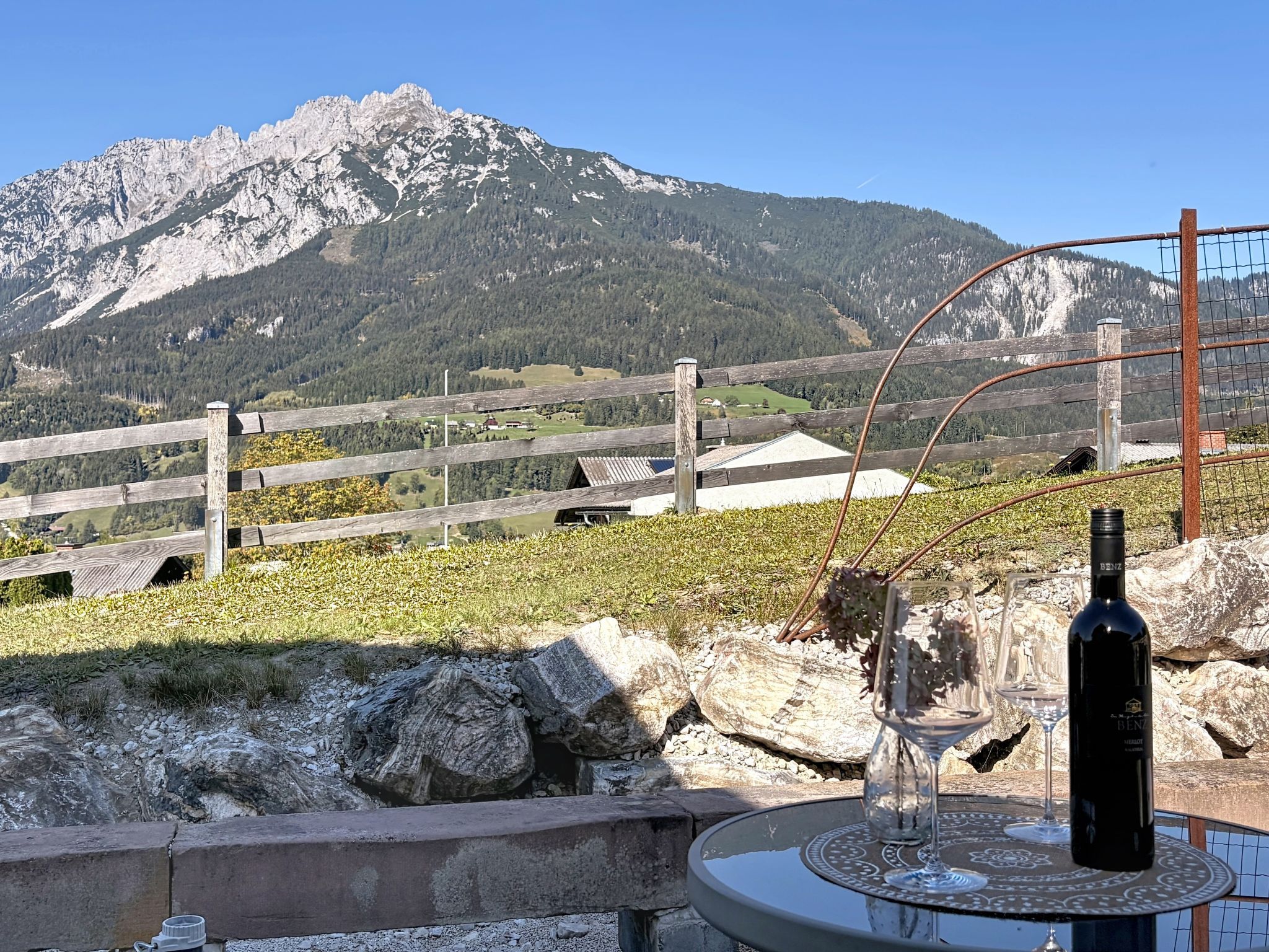 A bottle of wine and a glass on a table with a mountain view in the background.