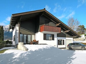 Ein modernes, zweistöckiges Haus mit geneigtem Dach und einem Balkon, ein Auto befindet sich auf der Auffahrt.