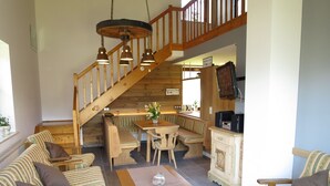 A cozy living room with a wooden staircase, a dining area, and a kitchen.