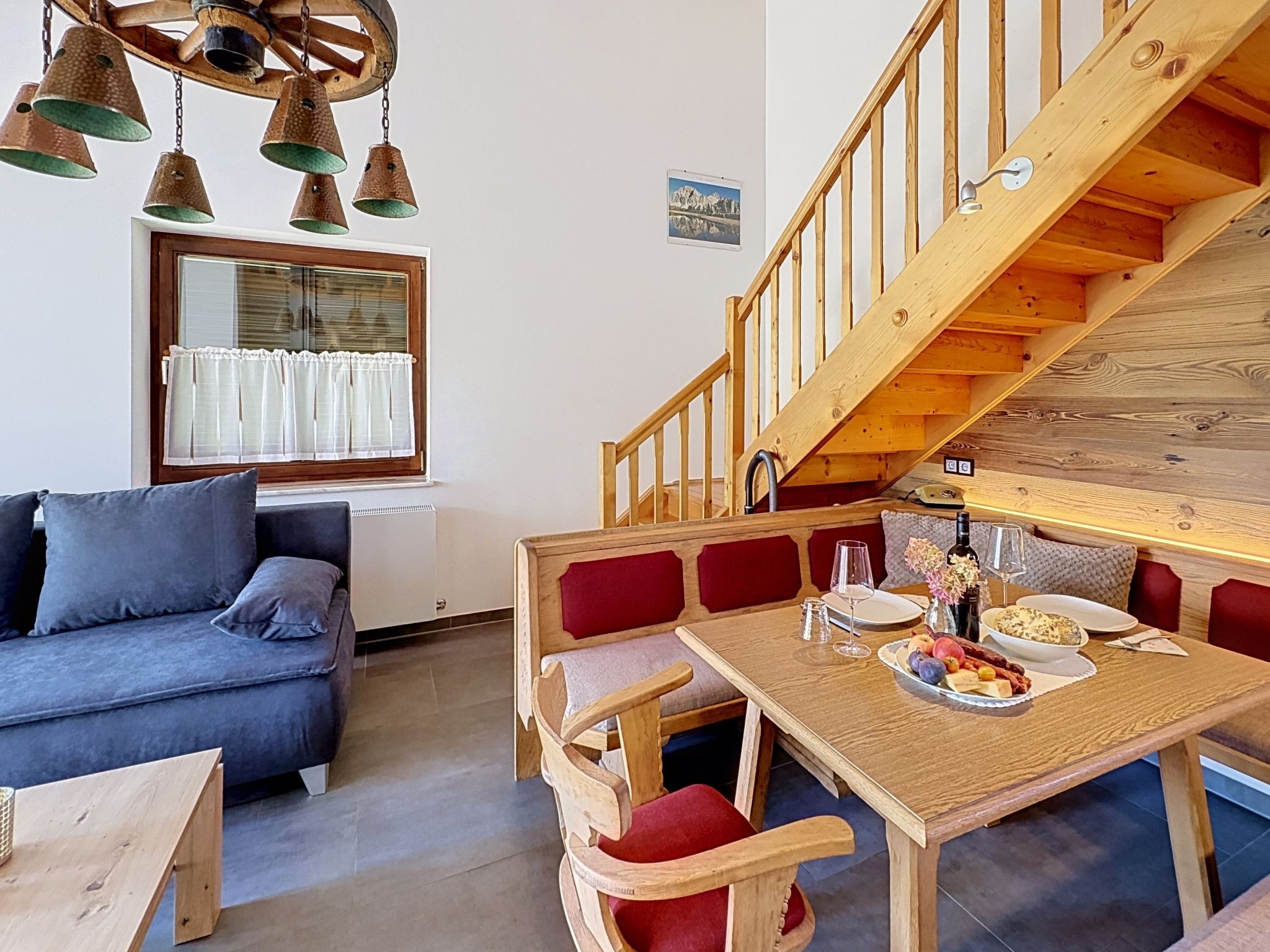 A cozy living area with a sofa, a dining table set with plates, glasses, and a bottle, and a wooden staircase.