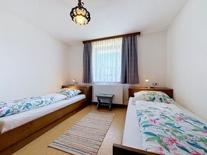 A bedroom with two single beds, a small table, a chair, a radiator, and a window with curtains. - Vacation home Jung by Interhome (Gröbming)