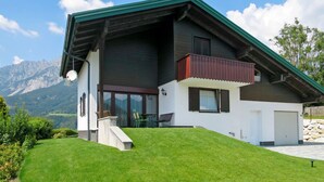 A modern two-story house with a green roof, a balcony, and a mountain view.