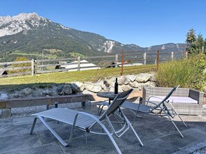 Ein Sitzbereich im Freien mit Metallstühlen und einem Tisch, mit Blick auf eine gebirgige Landschaft.