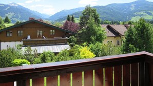 A wooden house with a balcony, surrounded by lush greenery and mountains in the background.