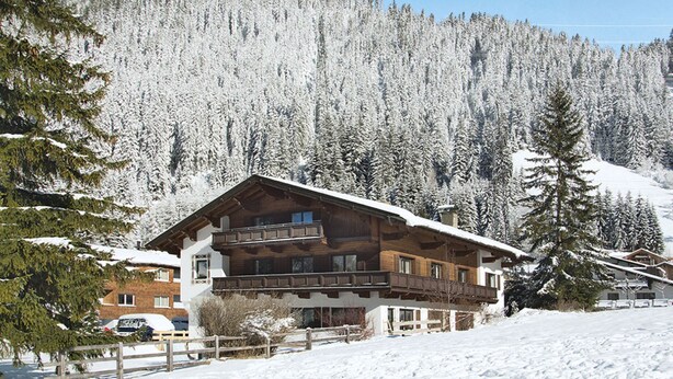 Una cabaña de madera con balcón, rodeada de árboles cubiertos de nieve y un paisaje montañoso.