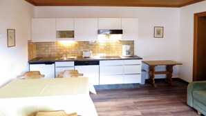 Una cocina compacta con armarios blancos, salpicadero de azulejos y una mesa de comedor de madera con sillas.