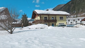 Ein zweistöckiges Gebäude mit Balkon, umgeben von verschneitem Gelände und Bergen im Hintergrund.