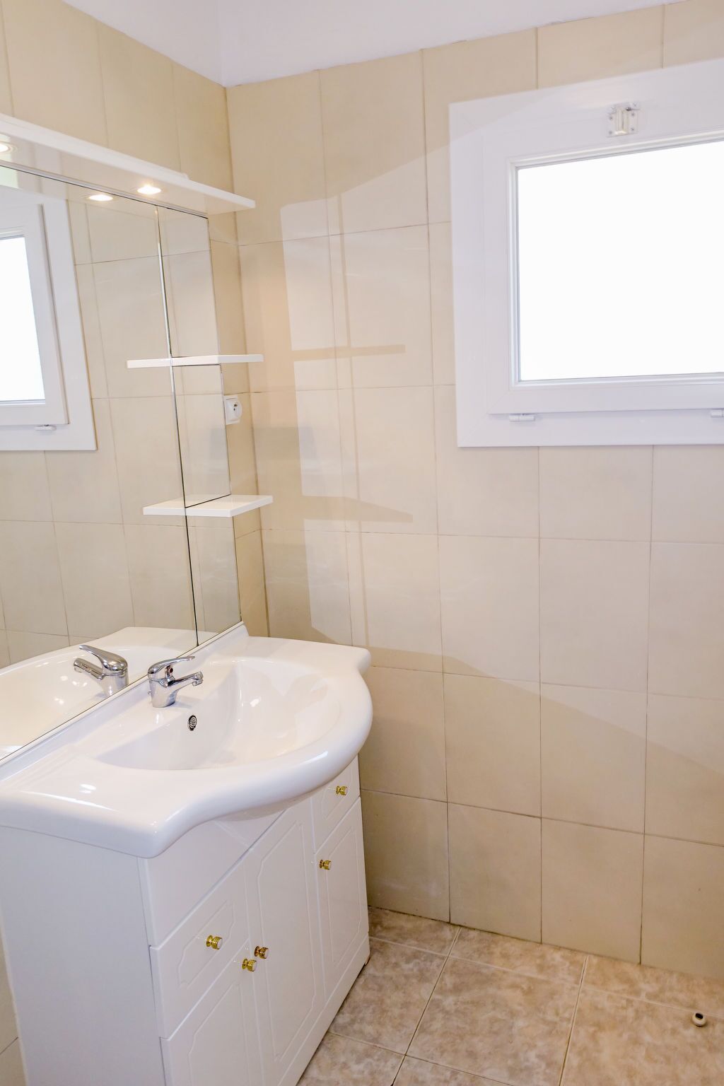 Ein Badezimmer mit einem weißen Waschbecken, einem Spiegel und einem Fenster.