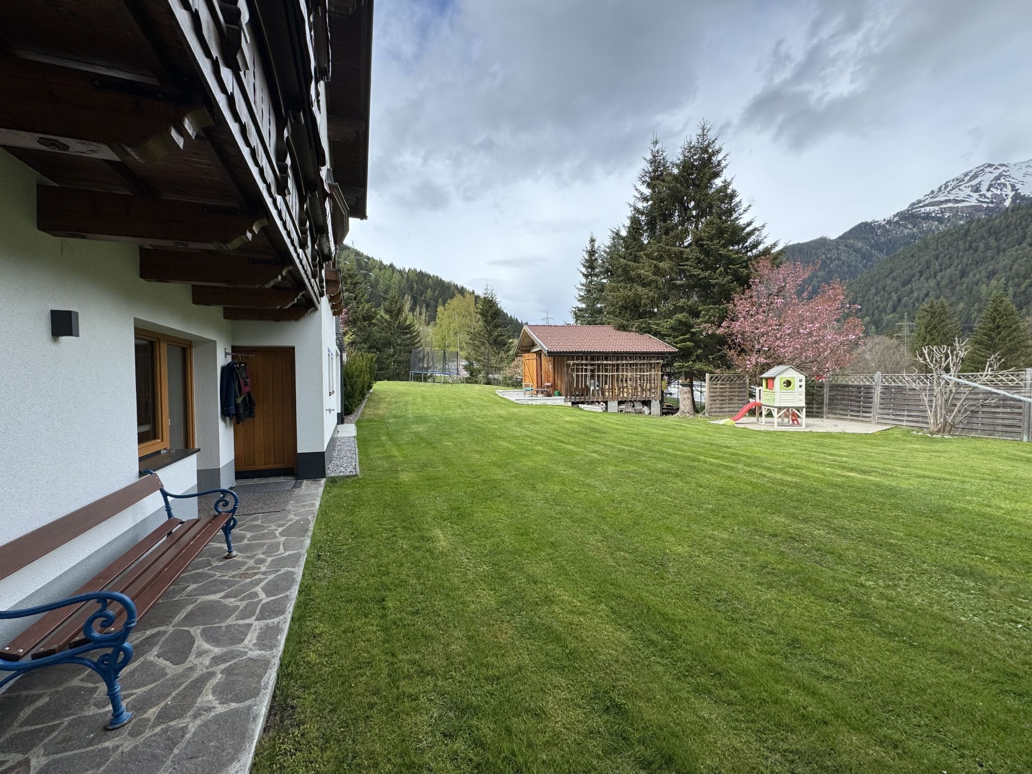 A well-maintained lawn, a wooden bench, a small wooden structure, and a mountain backdrop.