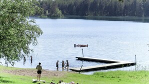 A lakeside scene with a dock extending into the water, surrounded by greenery and a forested area in the background. - Nedre Gärdsjö by Interhome (Rättvik)