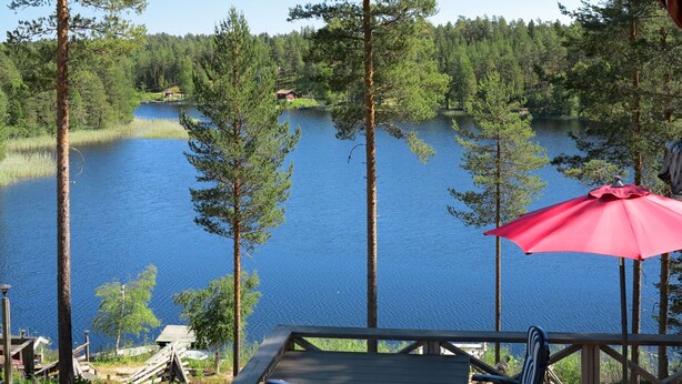 A wooden deck with a table and chairs overlooking a lake, surrounded by trees. - Nedre Gärdsjö by Interhome (Rättvik)