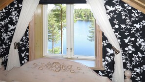 A bedroom with a bed, a window with a view of a lake and trees, and floral wallpaper. - Nedre Gärdsjö by Interhome (Rättvik)