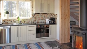 A modern kitchen with white cabinets, a tiled backsplash, a built-in oven, a coffee maker, and a wood-burning stove. - Nedre Gärdsjö by Interhome (Rättvik)